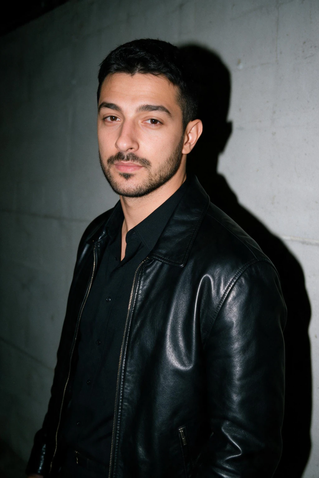 AI hard flash photo of a man with shoulders angled against a plain dark concrete wall, one crisp hard shadow behind him, generated from one selfie